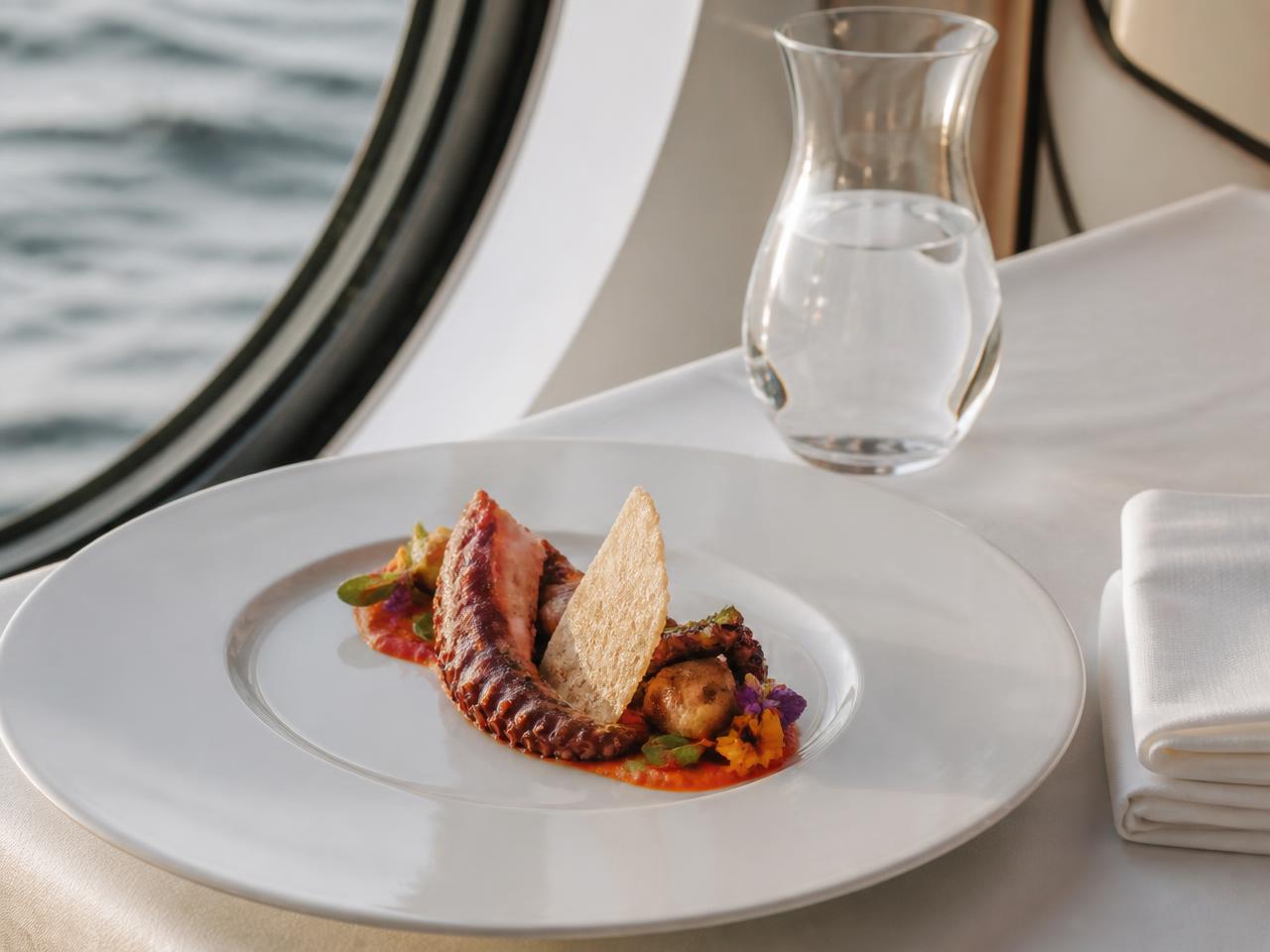 Plato de autor con mariscos servido junto a un ojo de buey con vista al mar